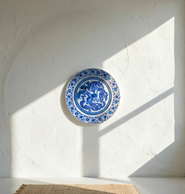 Blue and white decorative iznik plate on a white wall with sunlight casting shadows