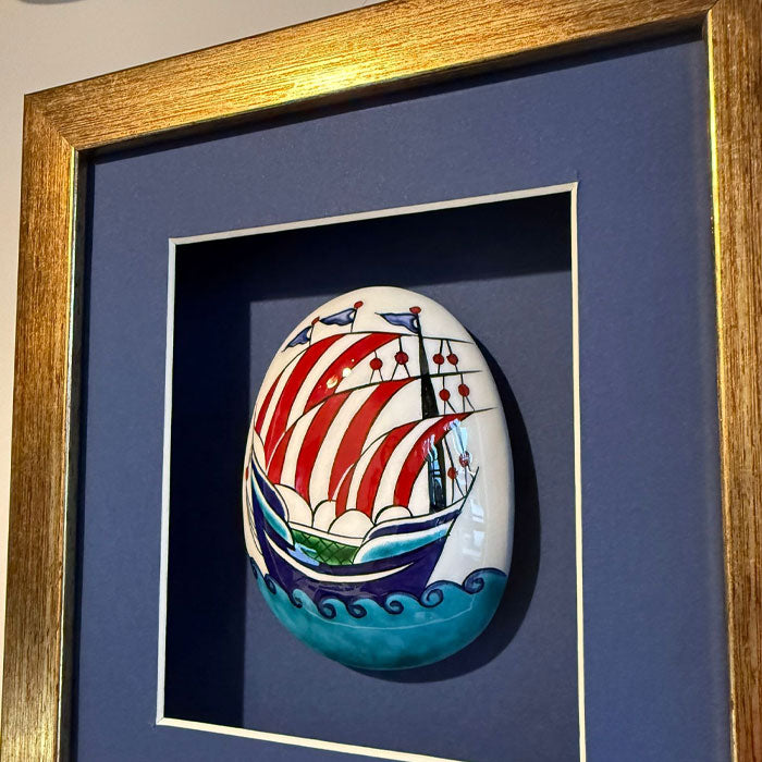 Framed artwork of a decorative stone with a ship design on a blue background